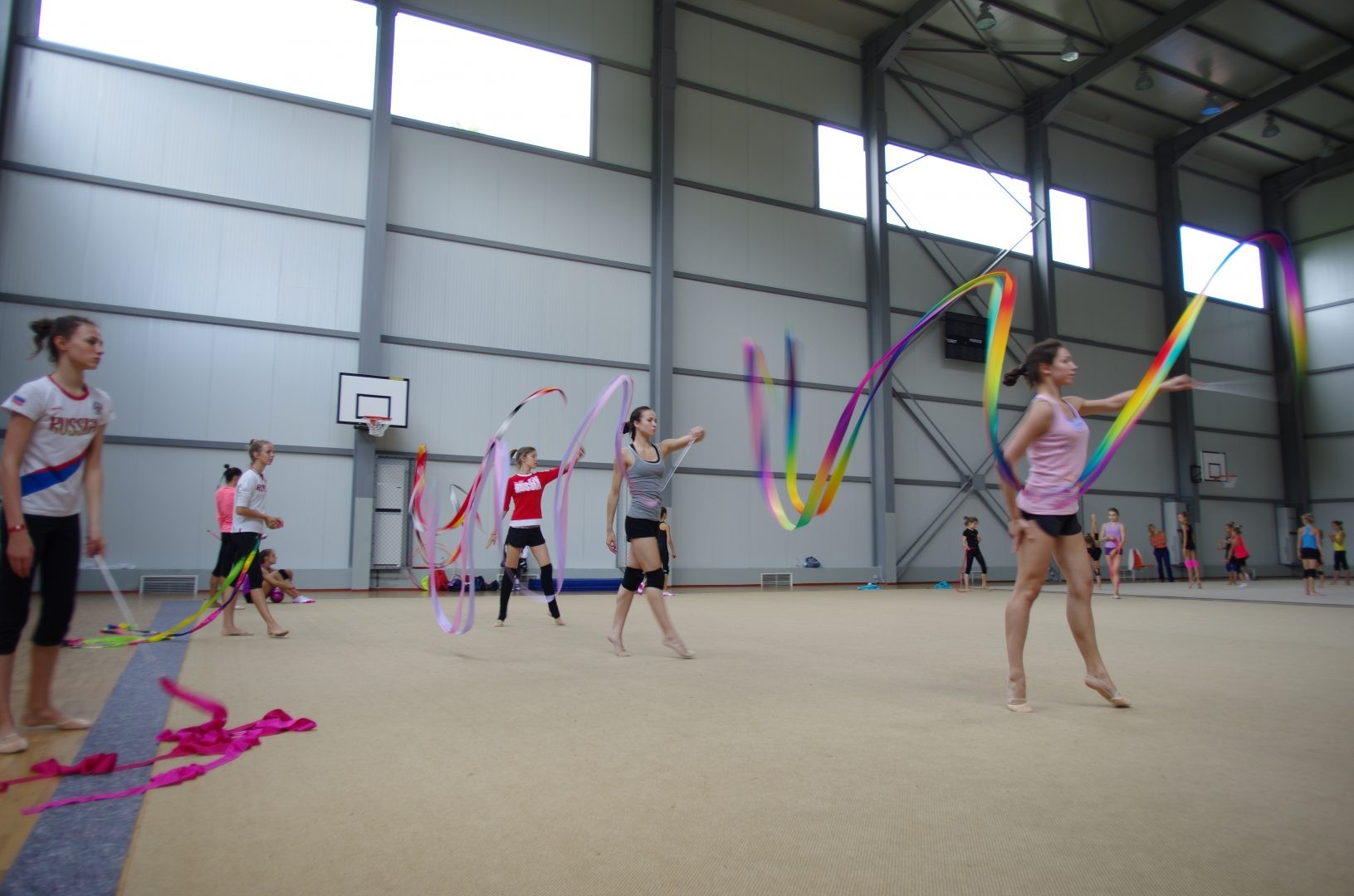 Athletes practicing rhythmic gymnastics with ribbons in an indoor hall during a training camp session