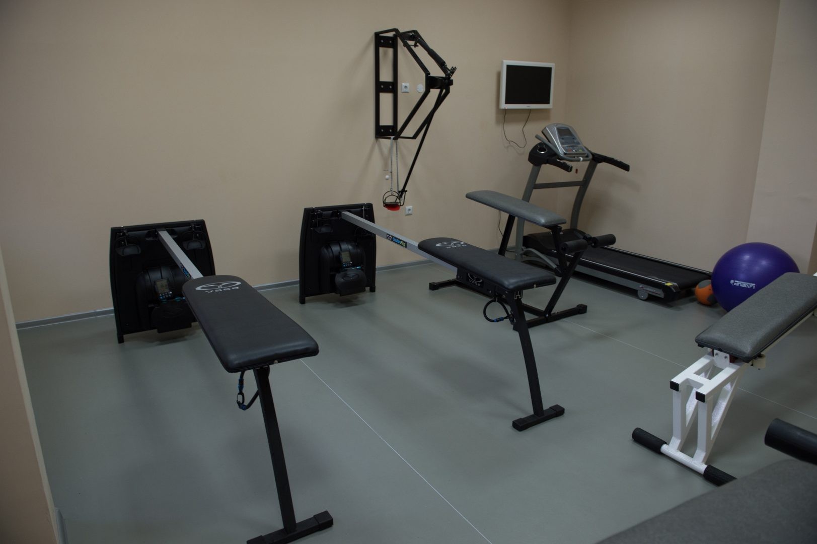Small training room with benches, treadmill, wall bars, and exercise balls for athlete workouts