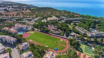 Luftaufnahme eines Sportkomplexes an der Küste mit Laufbahn, Feldern und Courts.