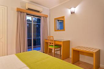 Gästezimmer mit Bett, Schreibtisch und Balkontür.