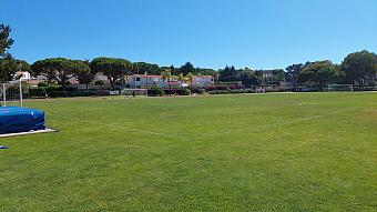 Rasen-Fußballplatz mit Toren und Laufbahn, mit wenigen Personen auf dem Feld.