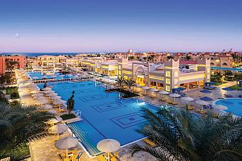 Weite Abendansicht einer Resortanlage mit großen Außenpools, Palmen und beleuchteten Gebäuden.