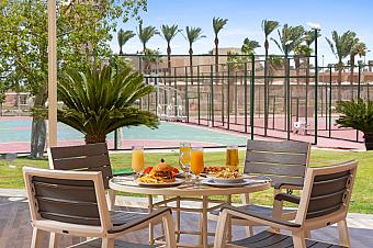 Breakfast table with juice and food set on terrace near tennis courts