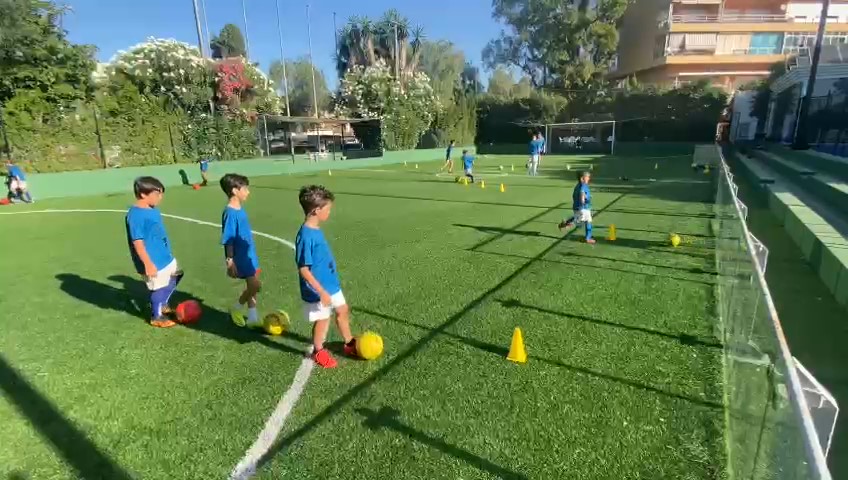 Kinder beim Fußballtraining mit Hütchen und Bällen auf Kunstrasen.