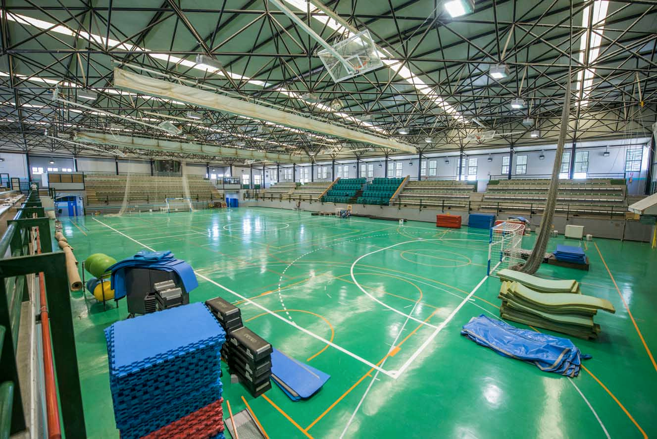 Sporthalle mit markierten Spielfeldern, Tribünen und Trainingsmatten.