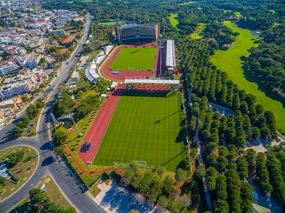 Luftaufnahme eines weitläufigen Sportkomplexes mit Stadionanlagen und mehreren Trainingsfeldern in grüner Umgebung. Die Anlage zeigt die Größe und Vielfalt der verfügbaren Venues für Camps und Turniere.