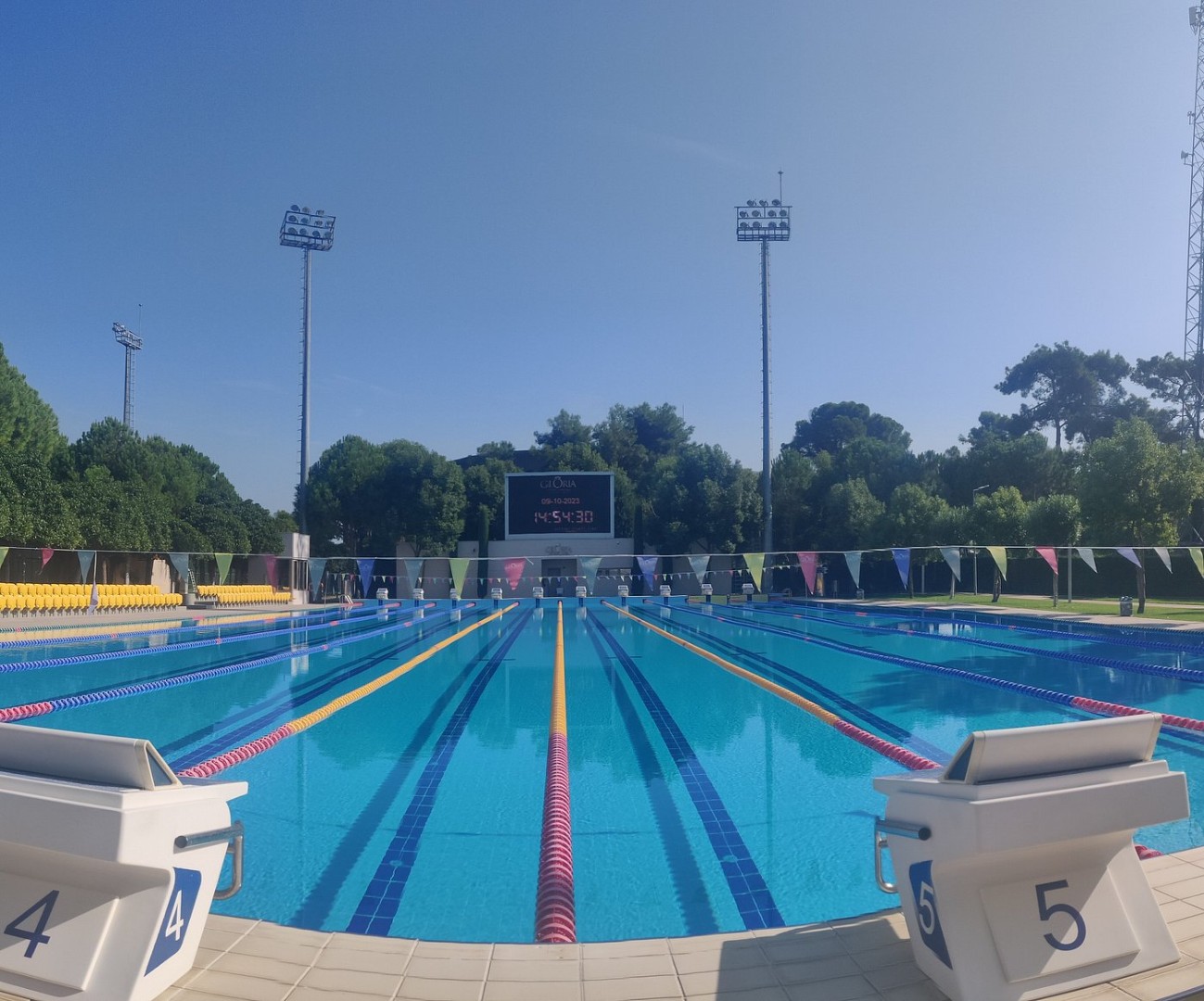 Außen-Schwimmbecken mit Startblöcken, Leinen, Anzeigetafel und Flutlicht.