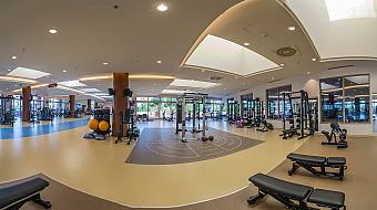 Panoramic view of a large fitness centre with dedicated strength areas, functional zones and extensive equipment. Bright interiors and wide spacing create an ideal environment for team workouts and individual training.
