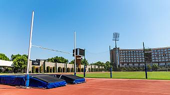 Leichtathletikbereich mit Hochsprungmatten neben Laufbahn und Rasenfeld auf einem Trainingscamp-Gelände.