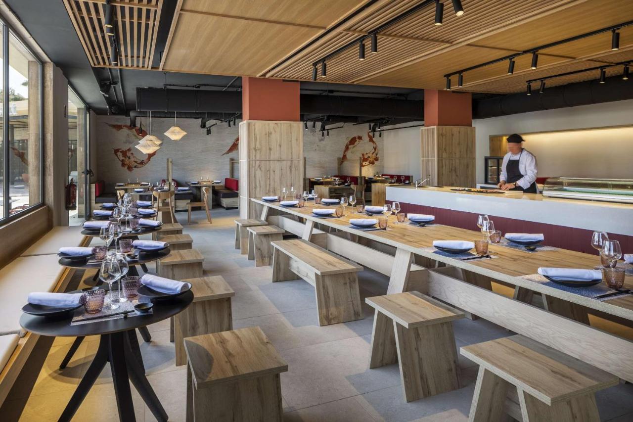 Intérieur de restaurant avec tables dressées, banquettes et comptoir de cuisine ouverte.