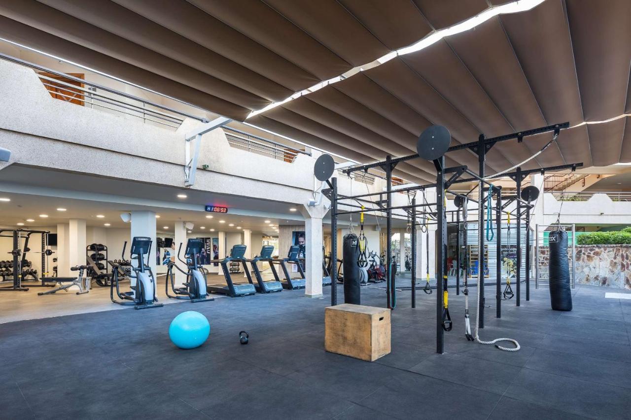 Espace d'entraînement en plein air avec appareils cardio, cage à squat fonctionnelle et sacs de frappe.