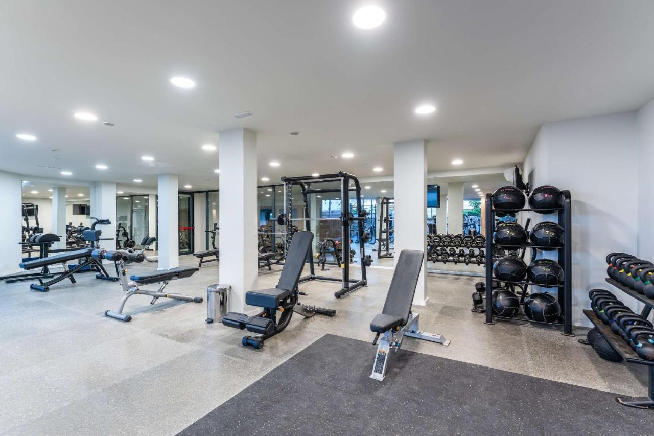Salle de sport avec appareils de musculation, poids libres et murs miroirs.