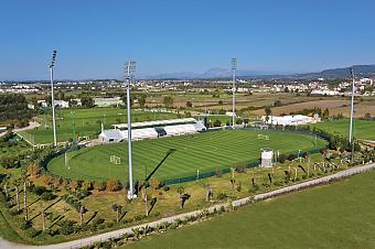Aerial view of the football stadium pitch with grandstand, floodlights and surrounding training fields.