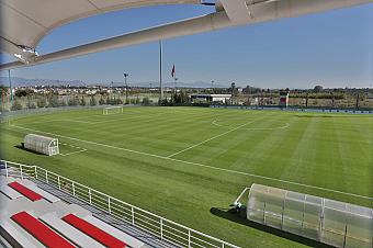 Daytime view of the football pitch from the grandstand with team benches and training setup.