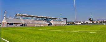 Football stadium stand beside a full-size grass pitch at the training camp venue.