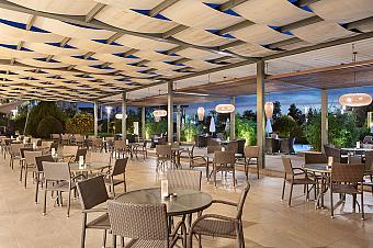 Covered outdoor terrace with tables and lounge seating in evening lighting.