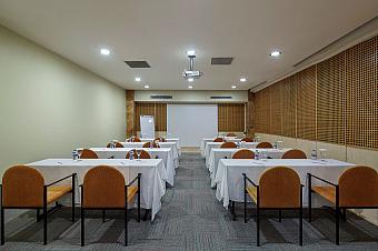 Meeting room set for presentations with rows of tables, projector and screen.
