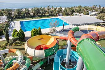 Water slides overlooking a large Olympic-style lap pool with sea views in the background.