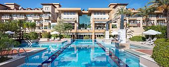 Outdoor hotel swimming pool with sun loungers and terrace seating in front of the main building.