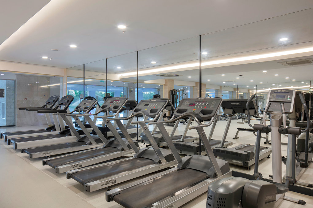 Fitnessraum mit Laufbändern und Crosstrainern vor einer Spiegelwand.