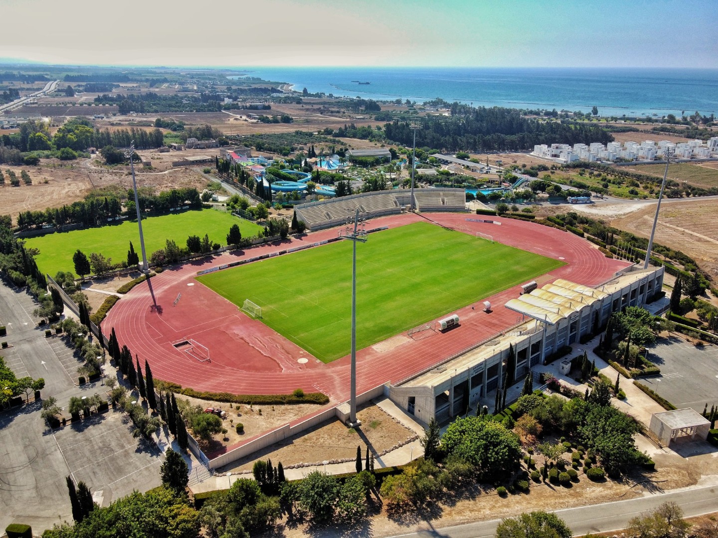 Aerial view of a stadium with running track and football field near the coast.