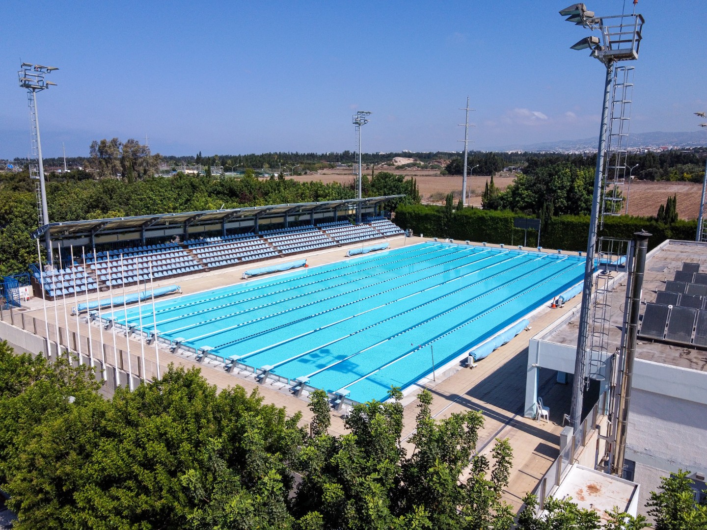 Aerial view of an outdoor lap pool with floodlights and spectator seating.