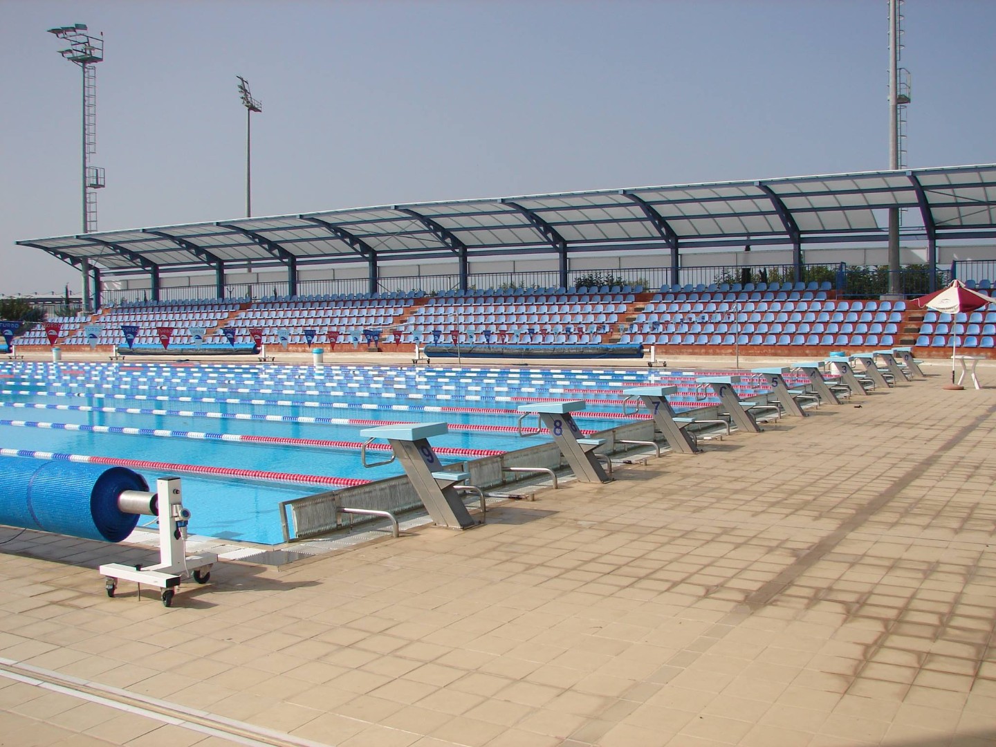 Outdoor lap pool with starting blocks and covered spectator seating.