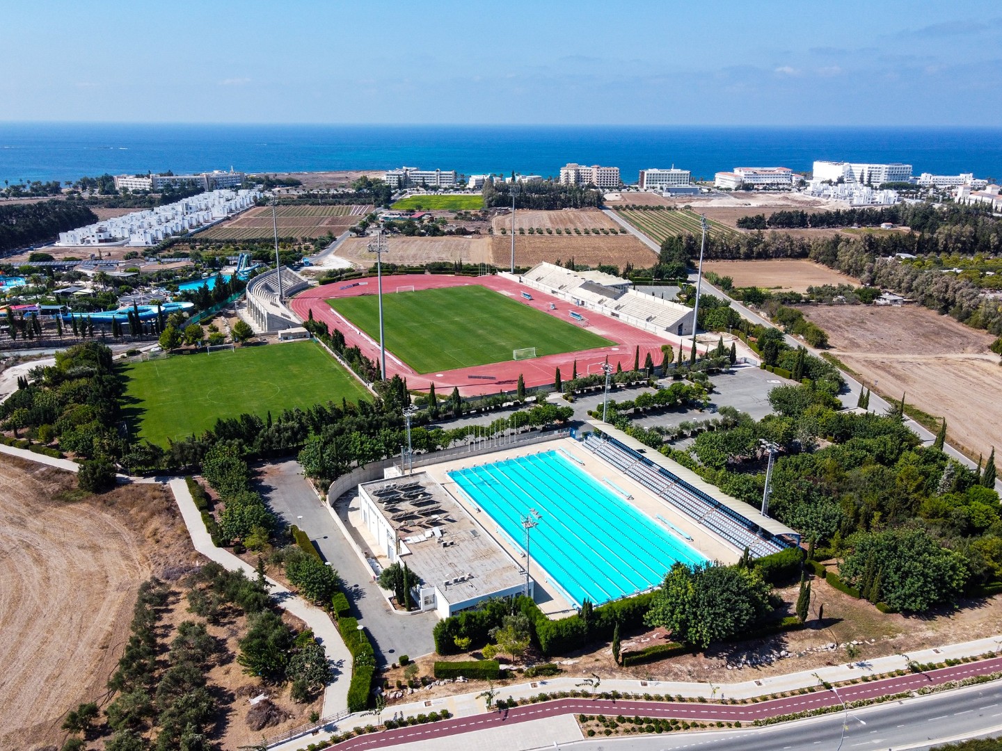 Aerial view of a sports complex with outdoor pool, stadium and coastal surroundings.
