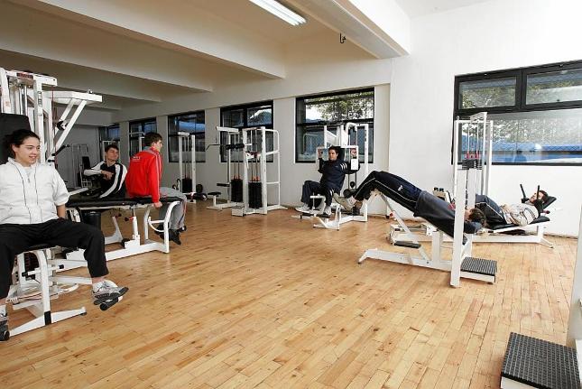 Salle de sport intérieure avec appareils de musculation et bancs, athlètes effectuant des exercices pendant le stage d'entraînement
