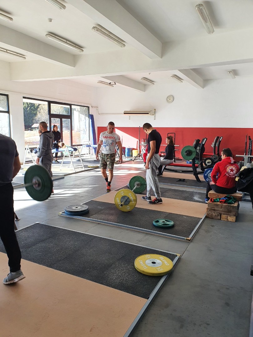 Zone d'haltérophilie avec plateformes et barres, athlètes effectuant des exercices de force pendant le stage d'entraînement