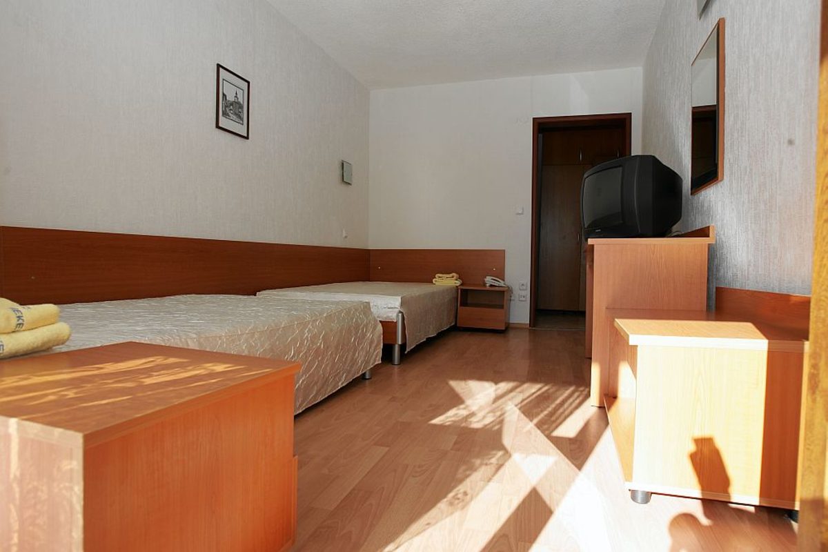 Chambre simple avec deux lits, commode et TV, logement pour les athlètes au stage d'entraînement