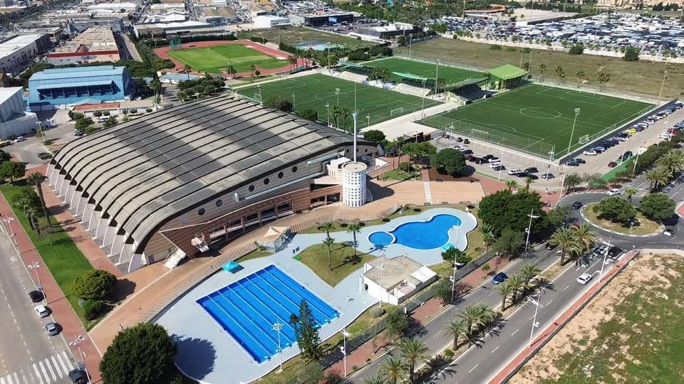Luftaufnahme eines Sportkomplexes mit Indoor-Arena, Bahnenbecken, Freizeitpool und Fußballplätzen.