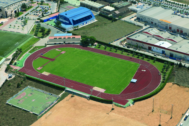 Luftaufnahme eines Leichtathletikstadions mit roter Laufbahn, grünem Innenfeld und umliegenden Sportgebäuden.