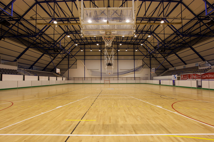 Zentraler Blick auf Indoorfeld mit Basketballkorb, Holzboden und hohem Bogendach.