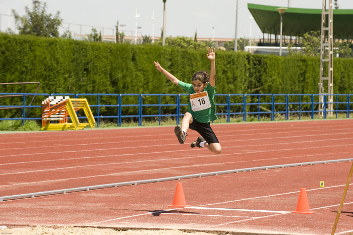 Athlet beim Weitsprung über die Sandgrube neben der Laufbahn, mit Markierungskegeln.