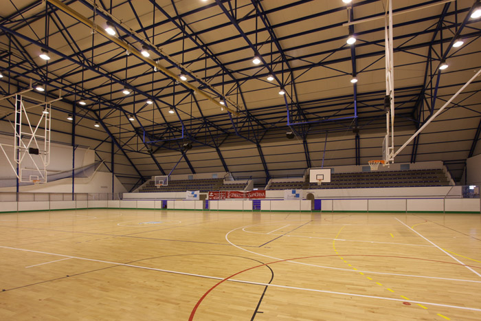 Leere Indoor-Mehrzweckarena mit Holzboden, Basketballkörben und Zuschauertribüne.