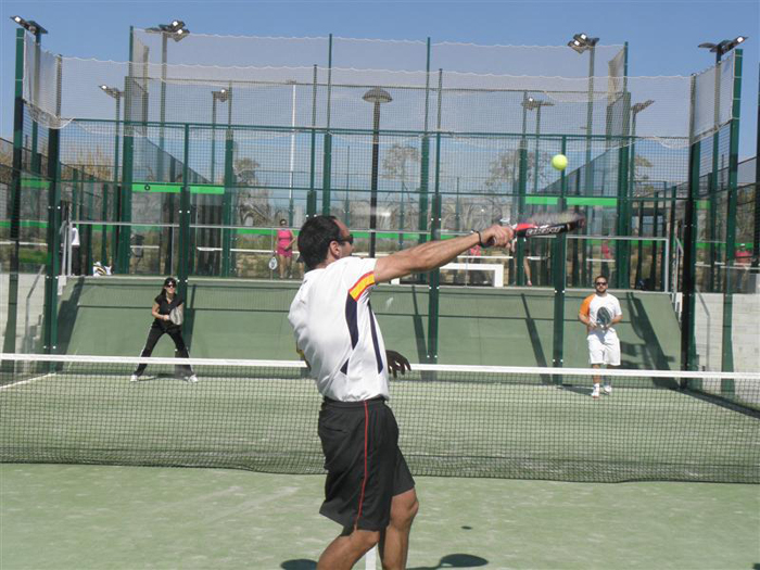 Padelplatz mit Glaswänden während eines Doppelballwechsels, Spieler am Netz.