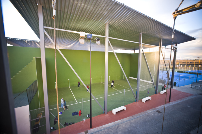Überdachter Racketsportplatz mit hohen grünen Wänden und Netzen, Spieler auf dem Feld.