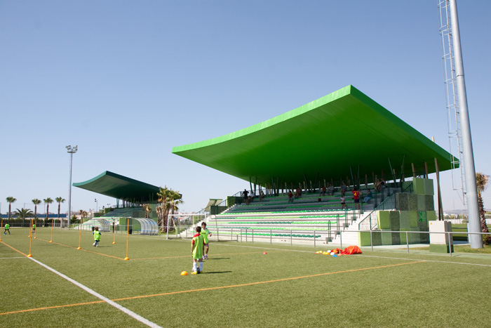 Fußballtraining auf einem Kunstrasenplatz vor großen überdachten grünen Tribünen, mit Hütchen für Übungsdrills.