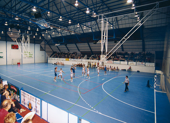 Indoor-Arena mit blauem Mehrzweckfeld während eines Teamspiels, mit Zuschauertribüne.
