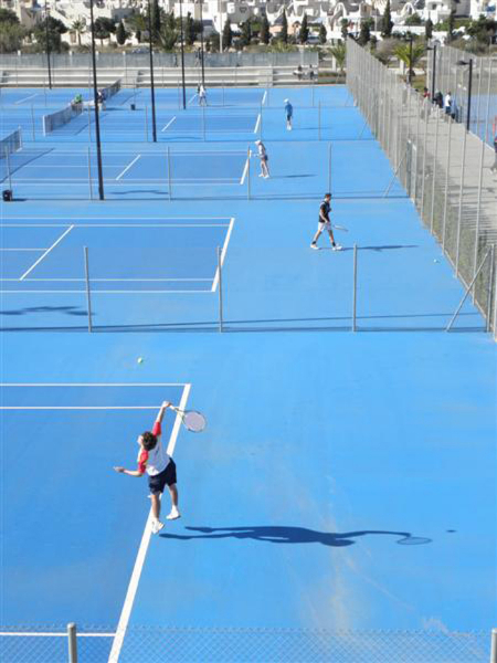 Outdoor-Tennisplätze mit blauem Belag und Zäunen, Spieler beim Training auf mehreren Plätzen.
