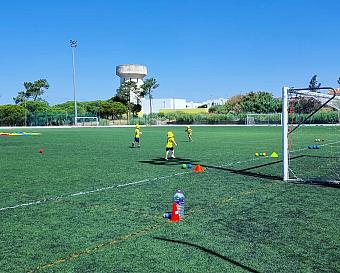 Children training on an outdoor football pitch with cones and small goals.