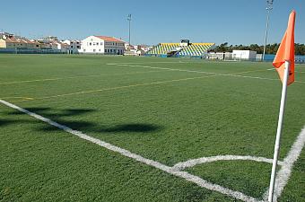Football pitch corner with artificial turf and a small grandstand.