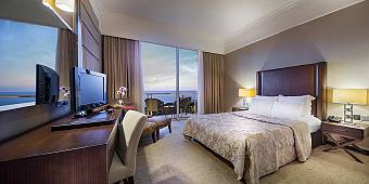 Hotel room with double bed, desk, TV, and balcony overlooking the sea