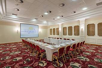 Conference room with U-shaped table setup, red chairs, and large projector screen