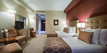 Hotel room with two double beds, TV, armchairs, and warm lighting