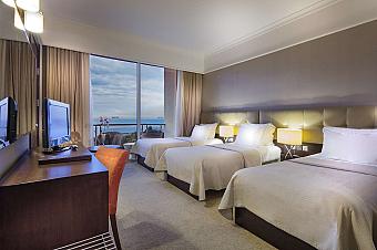 Hotel room with three single beds, desk, TV, and balcony with sea view
