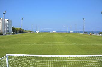 Football field with goalpost, floodlights, and ocean view in background