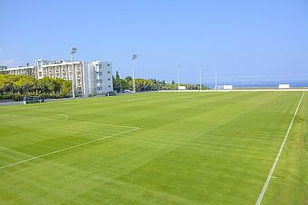 Expansive green football training pitch with resort buildings nearby