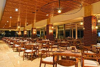 Restaurant with wooden chairs, set tables, and warm lighting under wooden ceiling